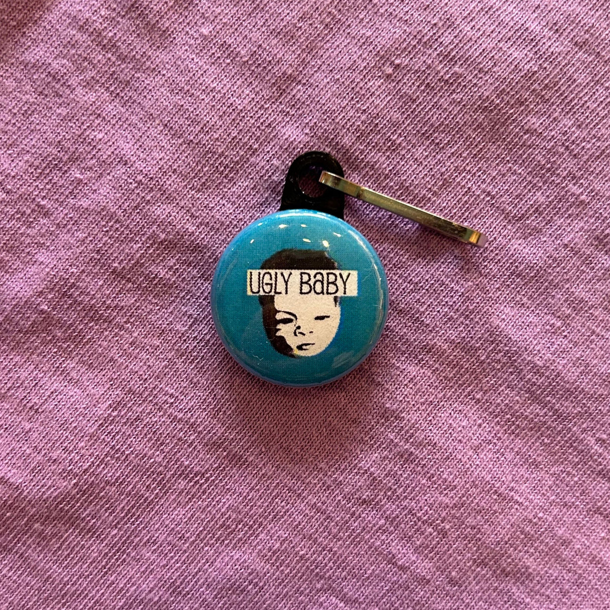 A zipper pull featuring the Ugly Baby logo and text that says "Ugly Baby" on a blue background. 