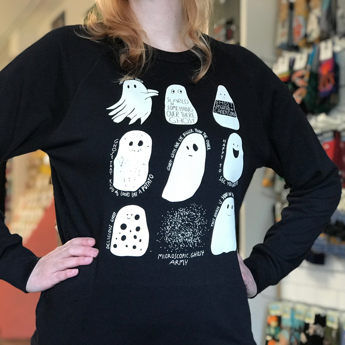 Person wearing a black long-sleeve shirt with white ghost illustrations in a store setting. 