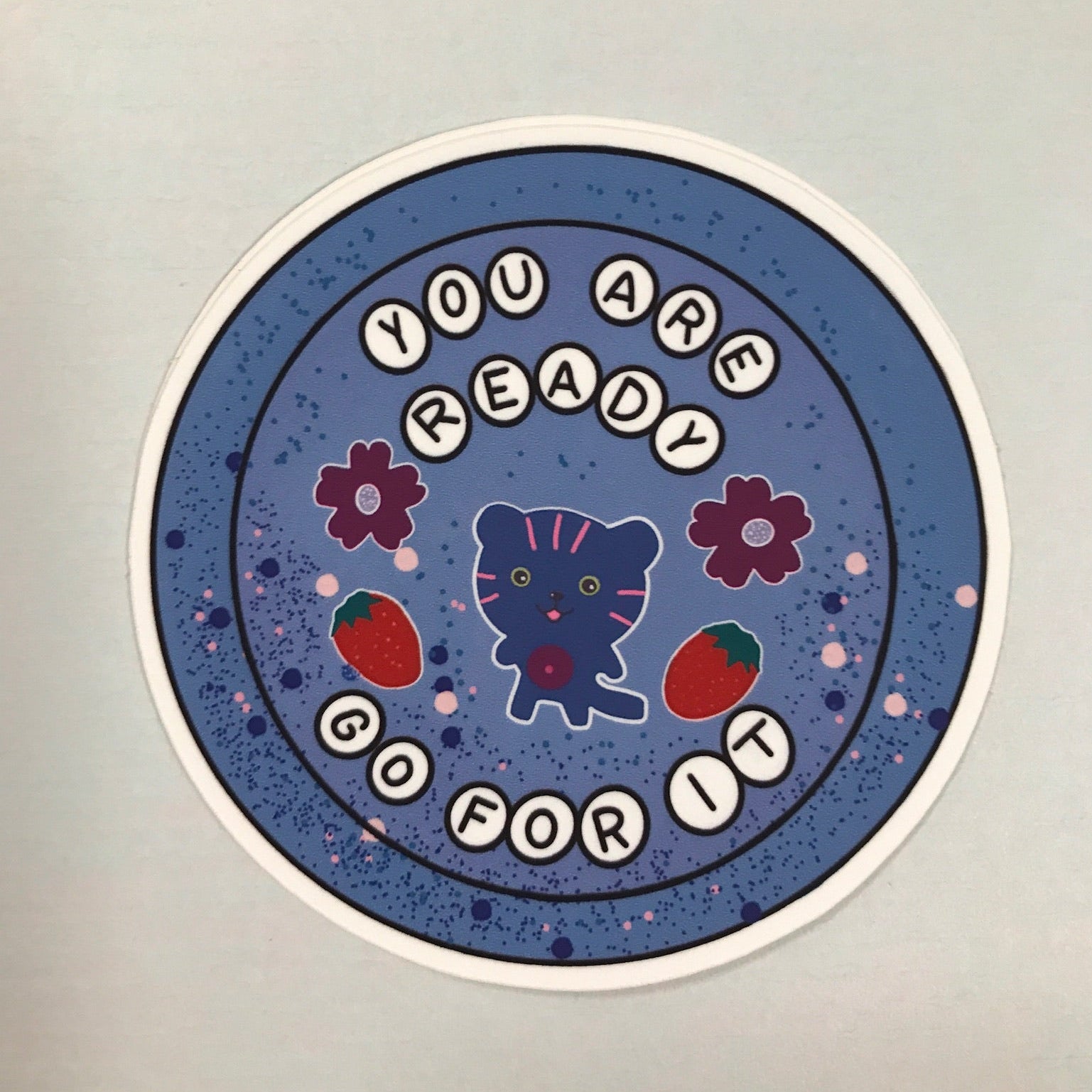 Circular sticker with motivational text and a cat illustration on a blue background