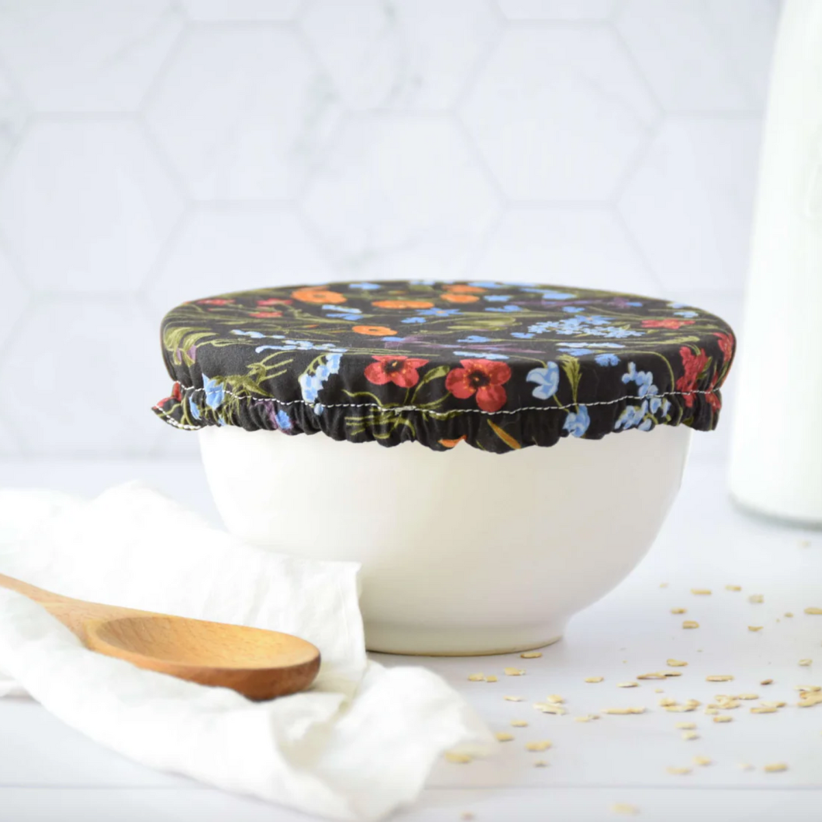 Floral-patterned lid on a white bowl with a wooden spoon and scattered oats on a light background
