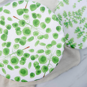 A round white plate or tray with a green watercolor leaf pattern, shown on a light neutral surface with another matching patterned item partially visible in the background.