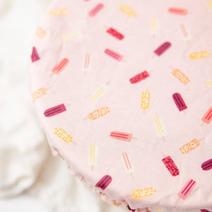 A close-up of a bowl cover, featuring a light pink background with a repeating pattern of colorful popsicle illustrations in red, yellow, and orange.