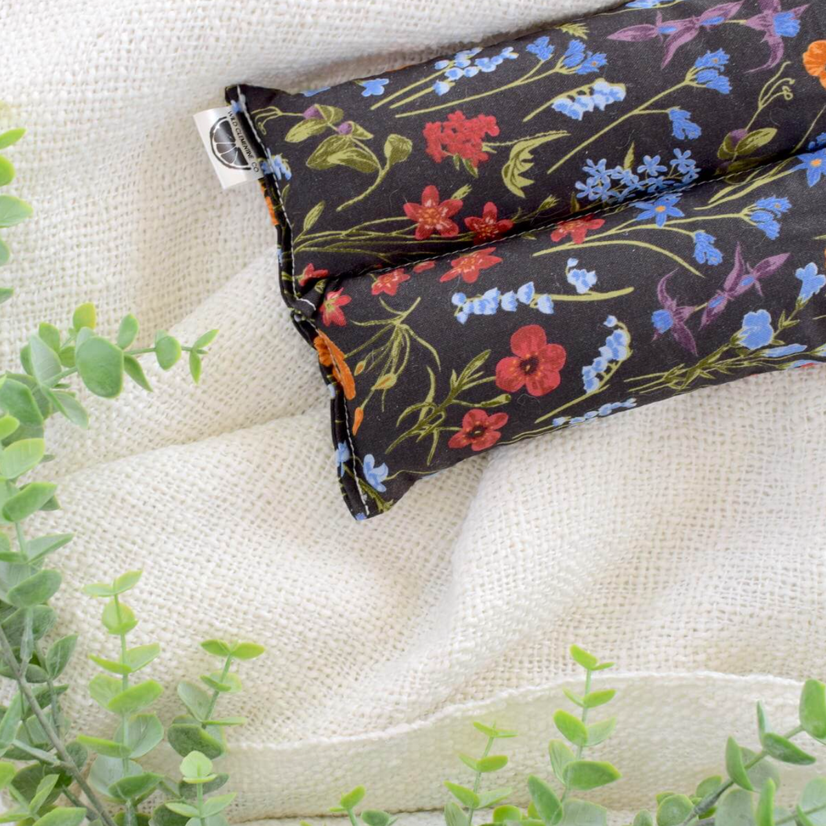 Floral-patterned hot/cold pack on a textured surface with green leaves.