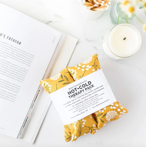 Hot and cold therapy pack with floral design on a white surface with a book and candle.