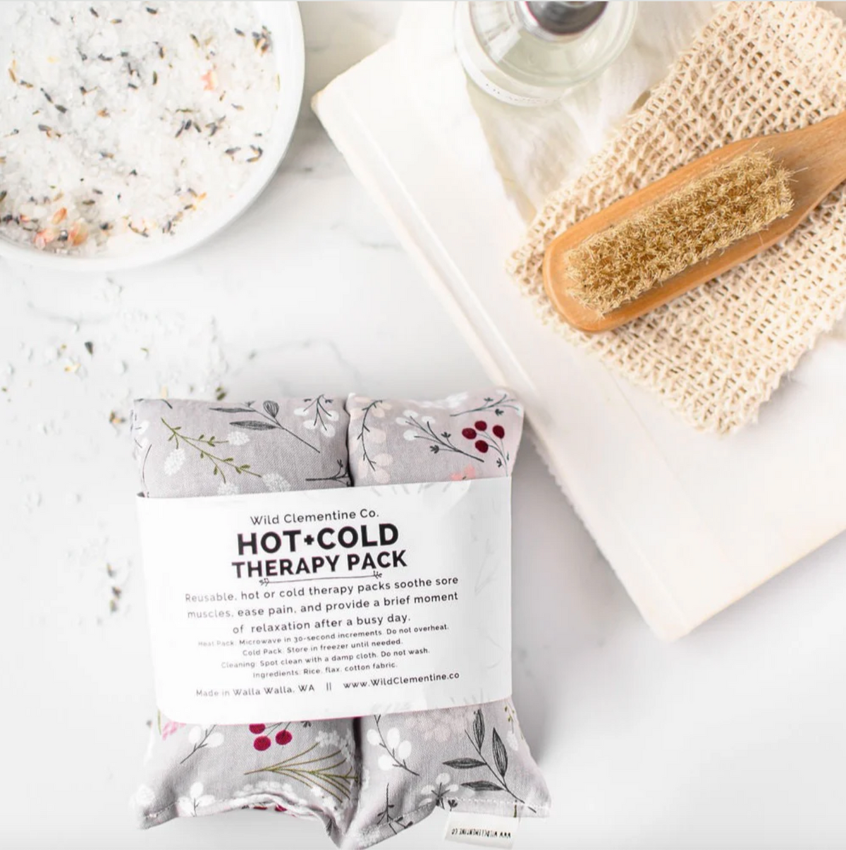 Hot and cold therapy pack with packaging on a marble surface with a wooden brush and bath salts.