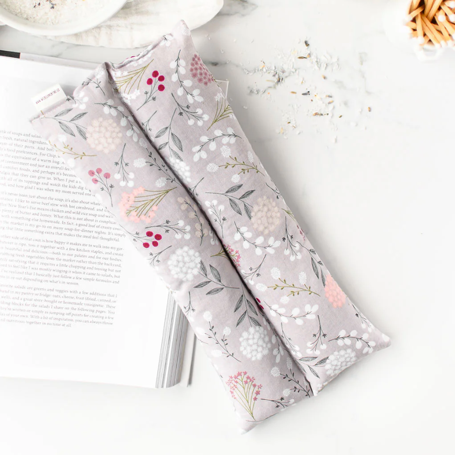 Floral-patterned hot/cold pack on a white surface with a book and bowl in the background