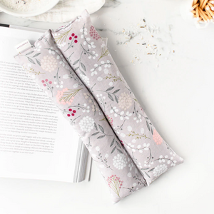 Floral-patterned hot/cold pack on a white surface with a book and bowl in the background