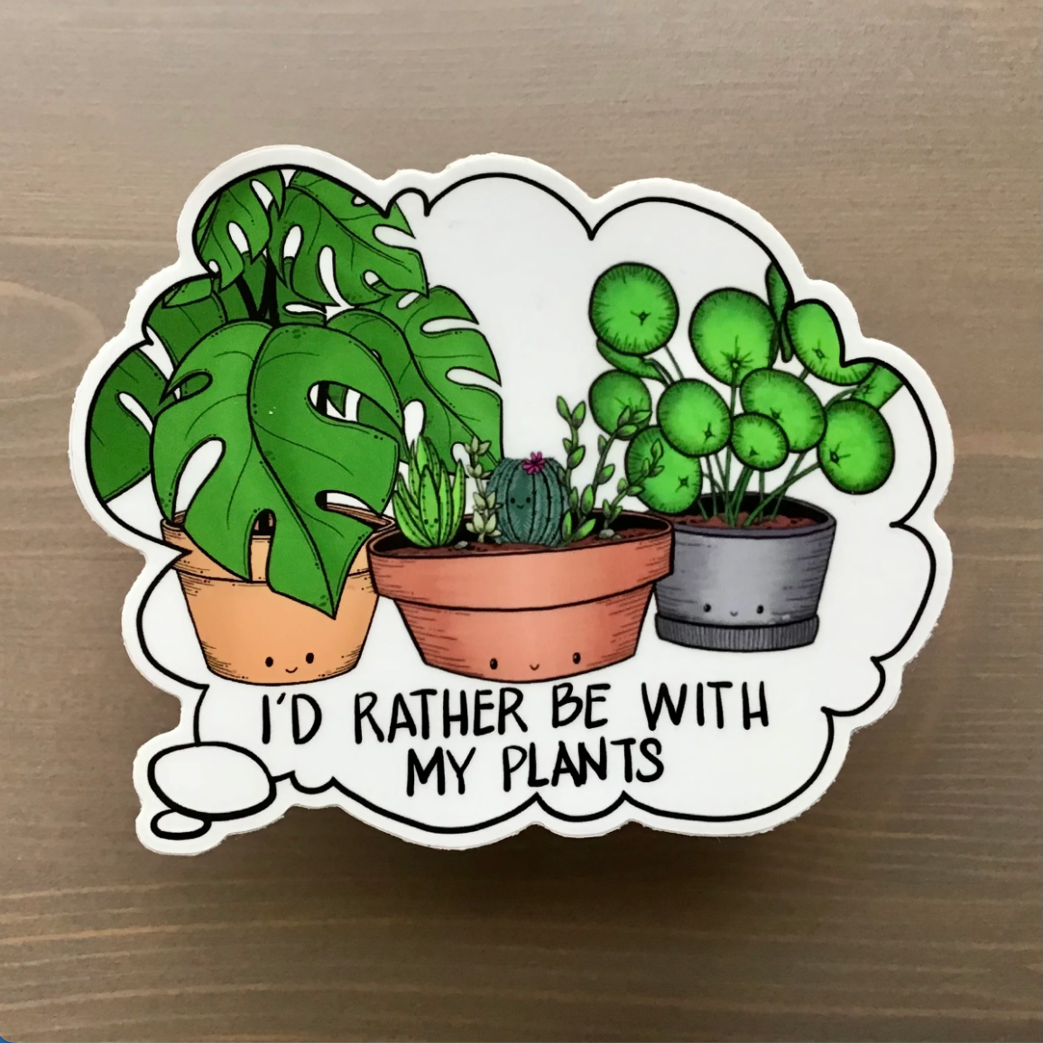 Sticker with cartoon plants and text 'I'd rather be with my plants' on a wooden surface