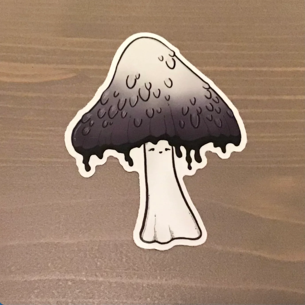 sticker of a mushroom with an ombre white to gray cap that is dripping with black ink. 