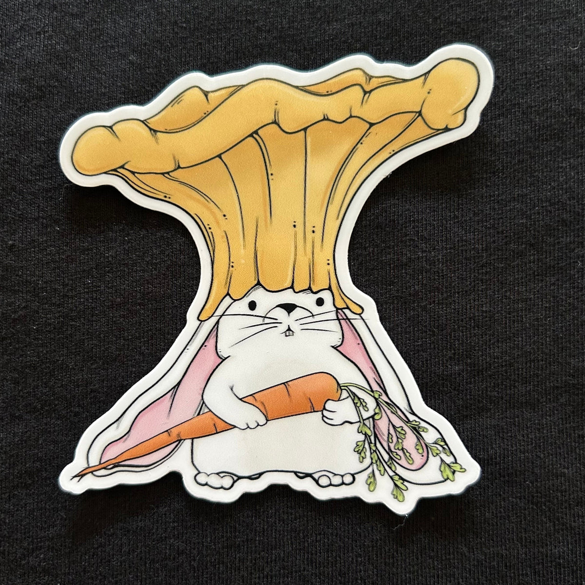 A sticker of a white rabbit wearing a chanterelle mushroom as a hat and holding a carrot. 