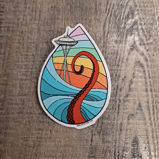 teardrop-shaped sticker featuring a rainbow background, the space needle, and a red octopus tentacle