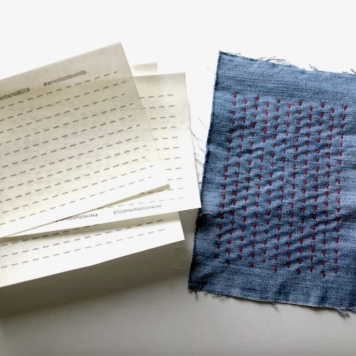 Textile sample with woven pattern next to a stack of papers on a light background