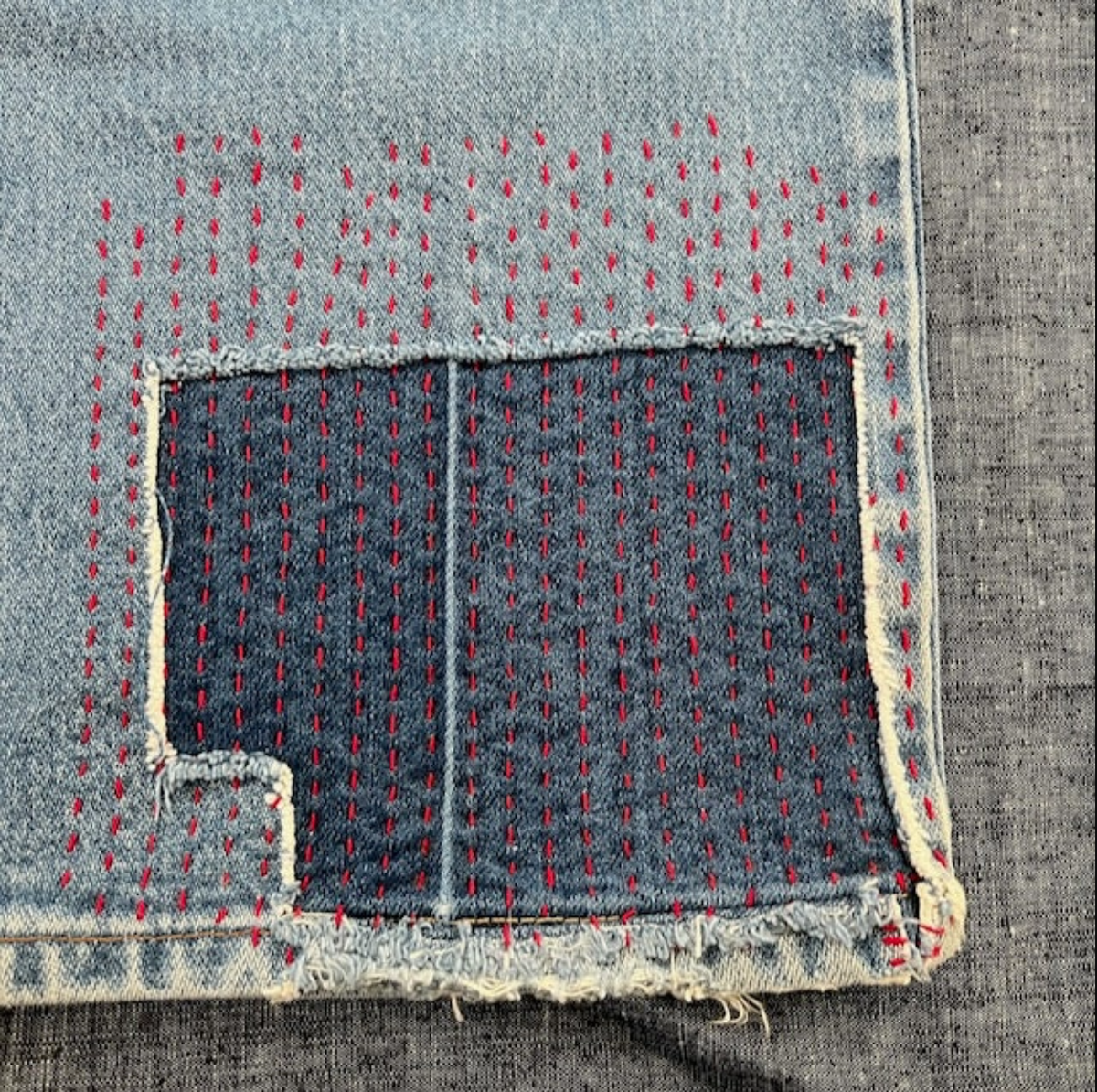 Close-up of denim fabric with a patch and red stitching