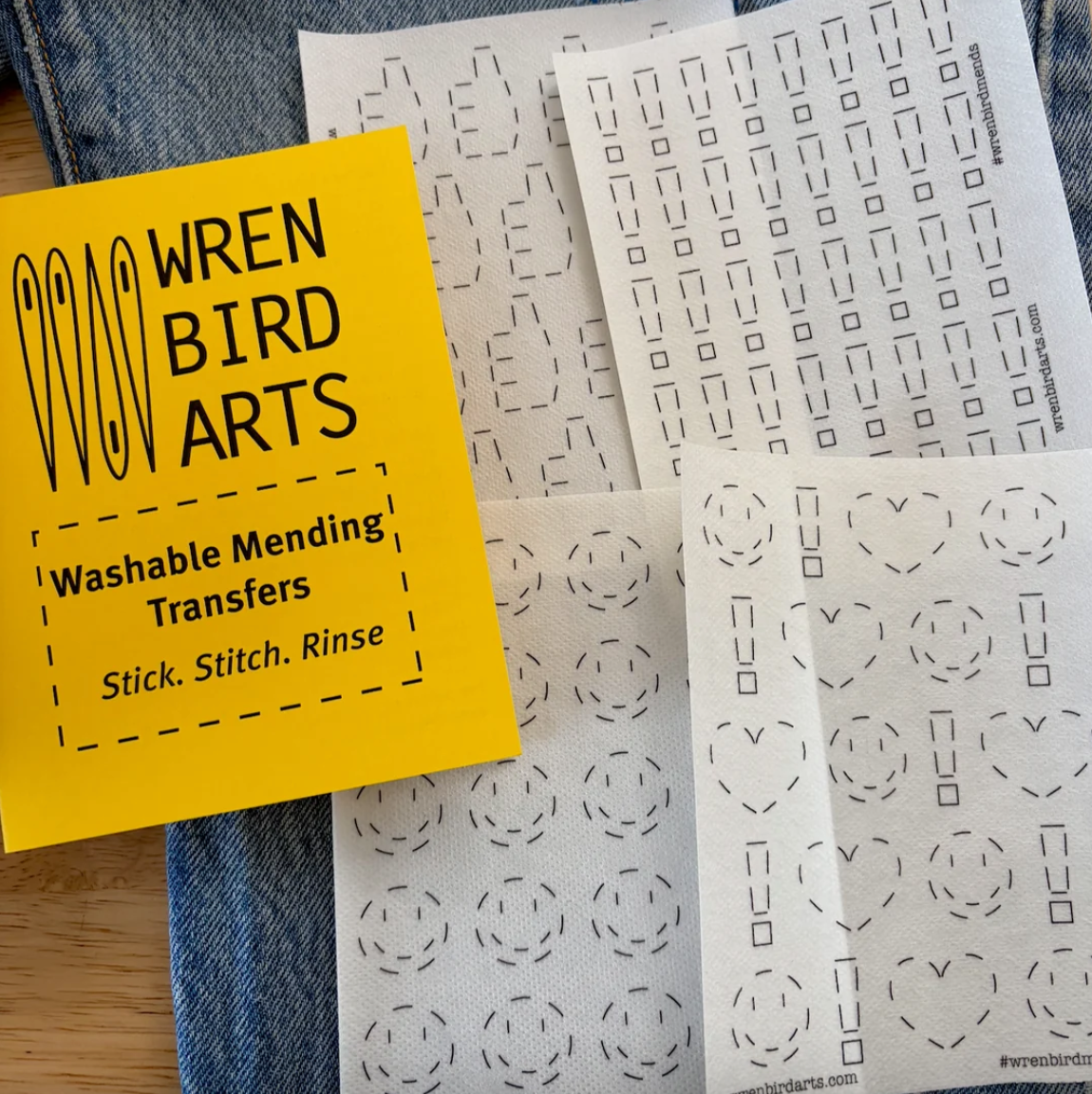 Four emoji-inspired mending transfer designs next to their yellow packaging on top of a pair of jeans. 