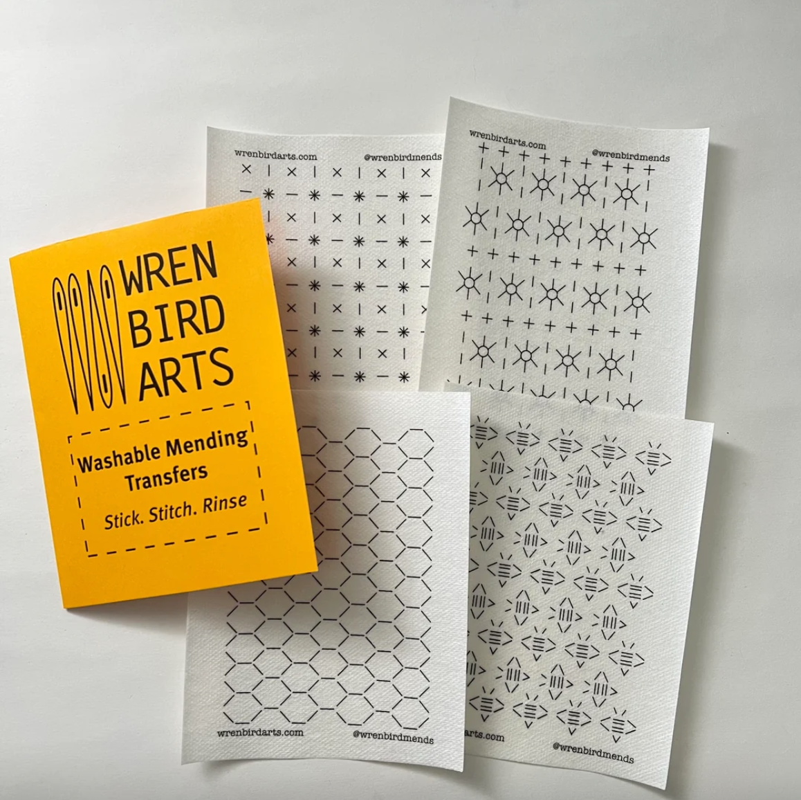 A set of washable mending transfers from Wren Bird Arts, including a bright yellow instruction card and several white pattern sheets with black stitch symbols, arranged on a light gray background.