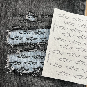 A stitched up example of a bat-themed embroidery transfer on black denim with a light blue denim patch underneath. 