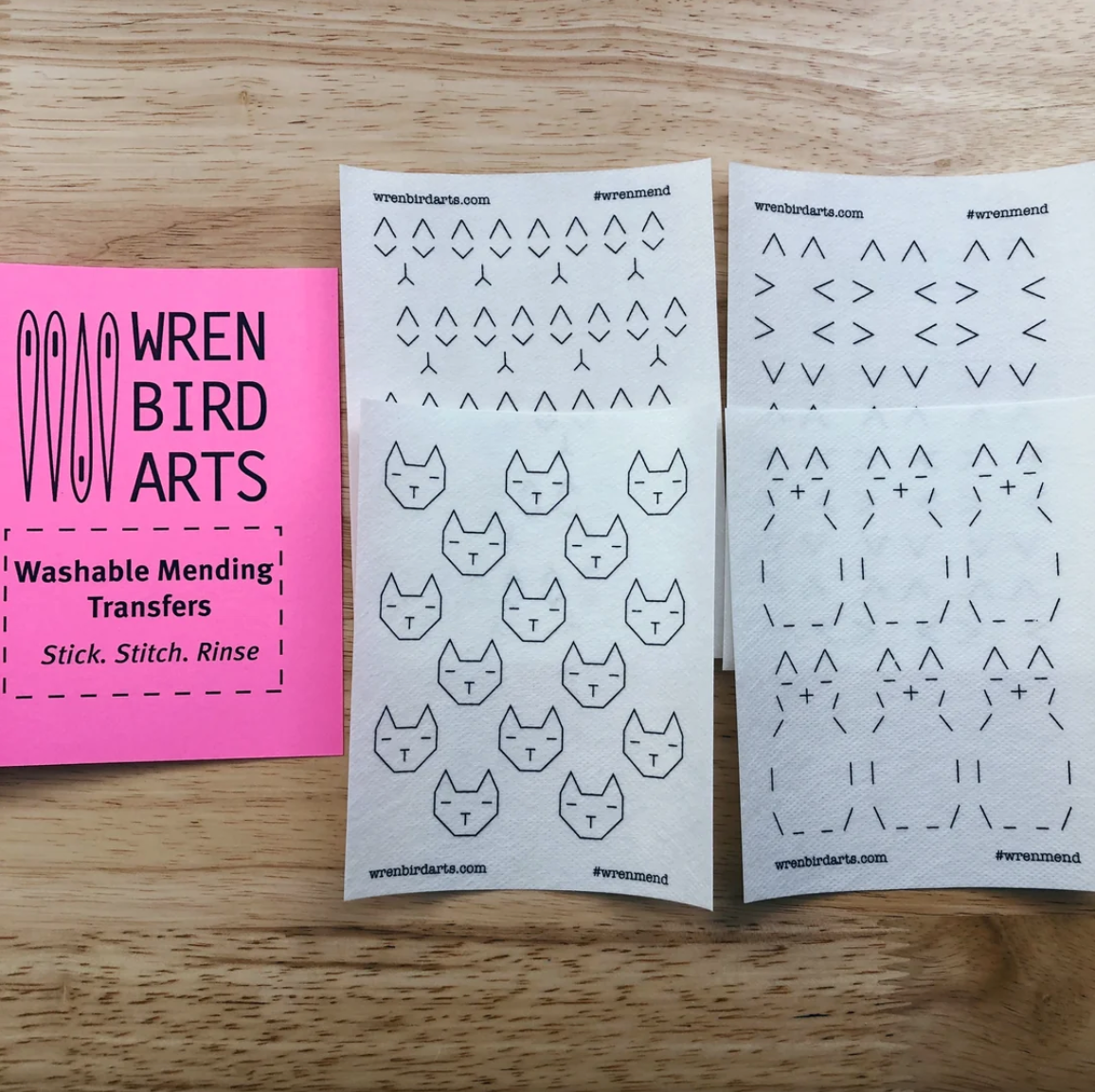 Four variations of cat-themed washable mending transfers from Wren Bird Arts on a wooden surface. 