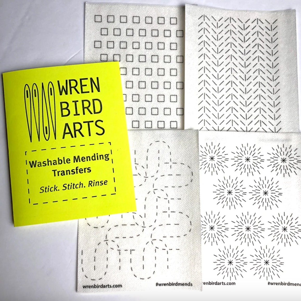 Four variations of washable mending transfers next to their bright yellow packaging with Wren Bird Arts branding
