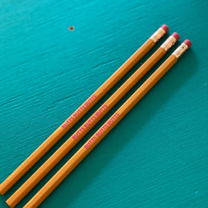 Yellow pencils with pink erasers are laying on a wood background painted turquoise. The pencils say "BUTTS BUTTS BUTTS" in bright pink text.