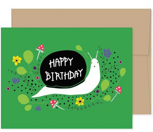 A greeting card with a bright green background. A surprised looking snail is carrying a shell that says "Happy Birthday" across his back. There are tiny mushrooms and illustrated flowers and leaves in the background.  The photo has a white background and the card is shown on top of a Kraft colored envelope. 