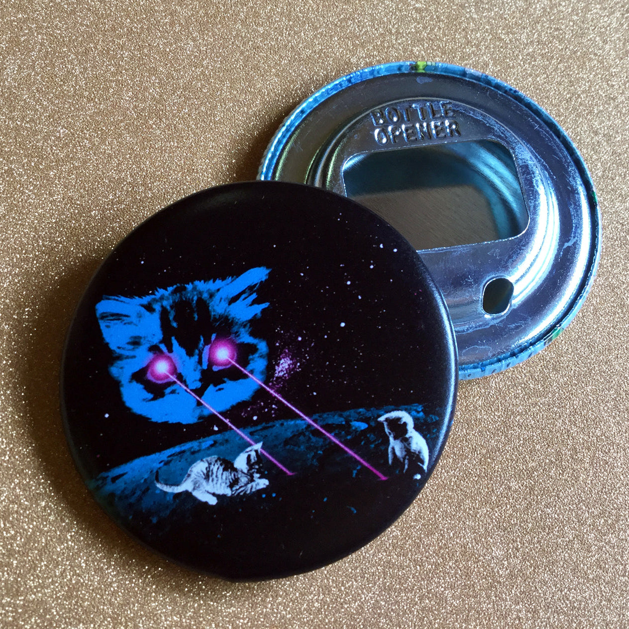 Round bottle opener with laser cat design against a gold glittery background. 