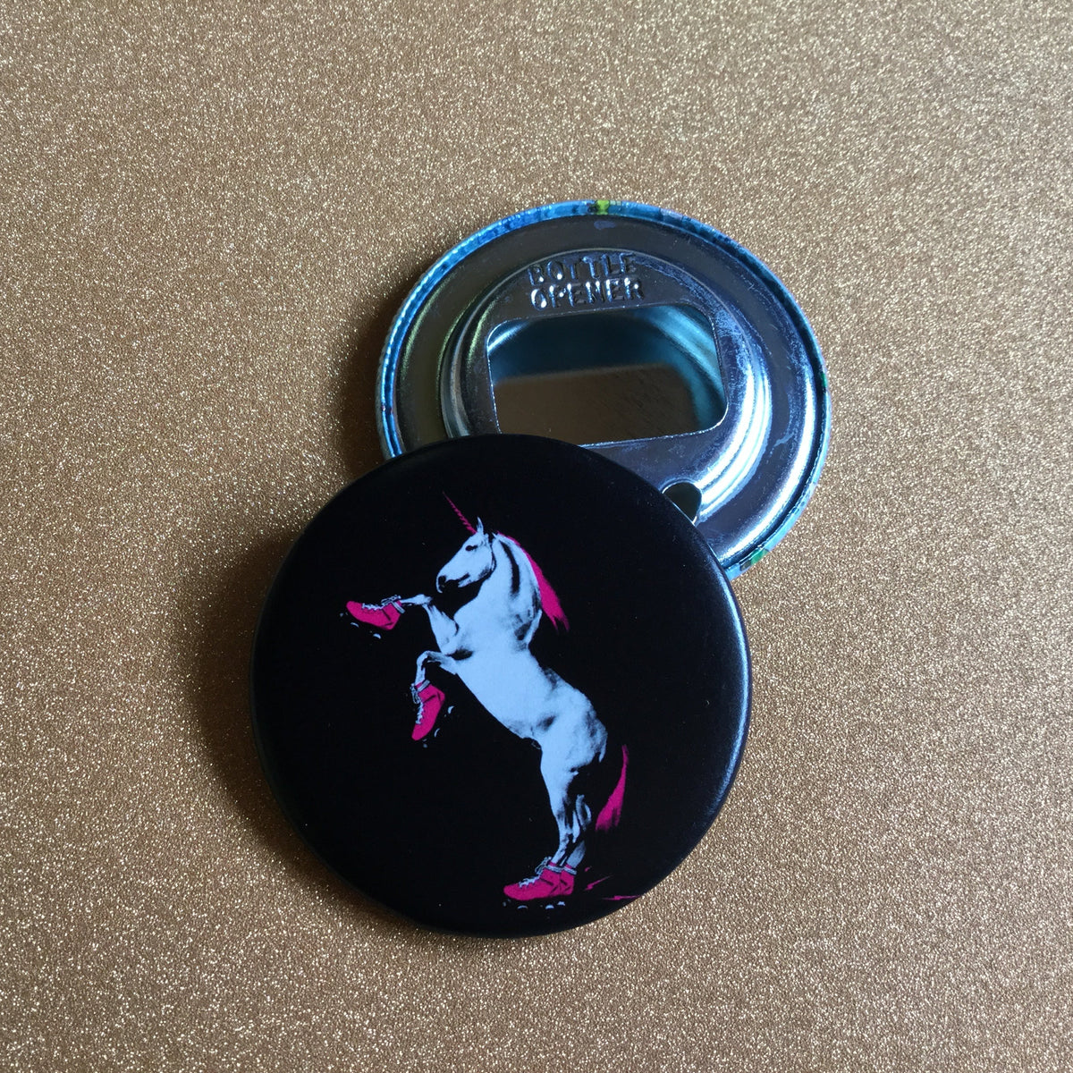 Black bottle opener with unicorn design on a glittery gold surface