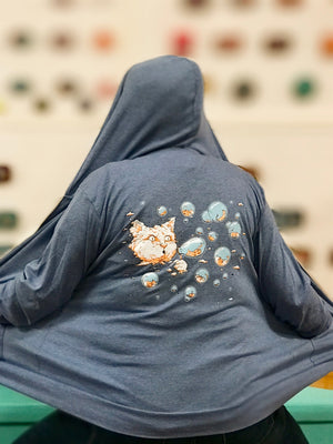 A light heathered blue hooded sweatshirt. On the back a cloud cat is blowing bubbles and inside the bubbles are sleeping kittens. 