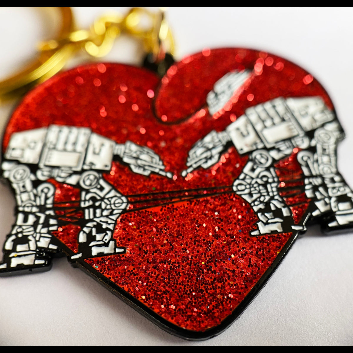 A red glittery keychain in the shape of a heart with an AT-AT from the Star Wars franchise design integrated into it.