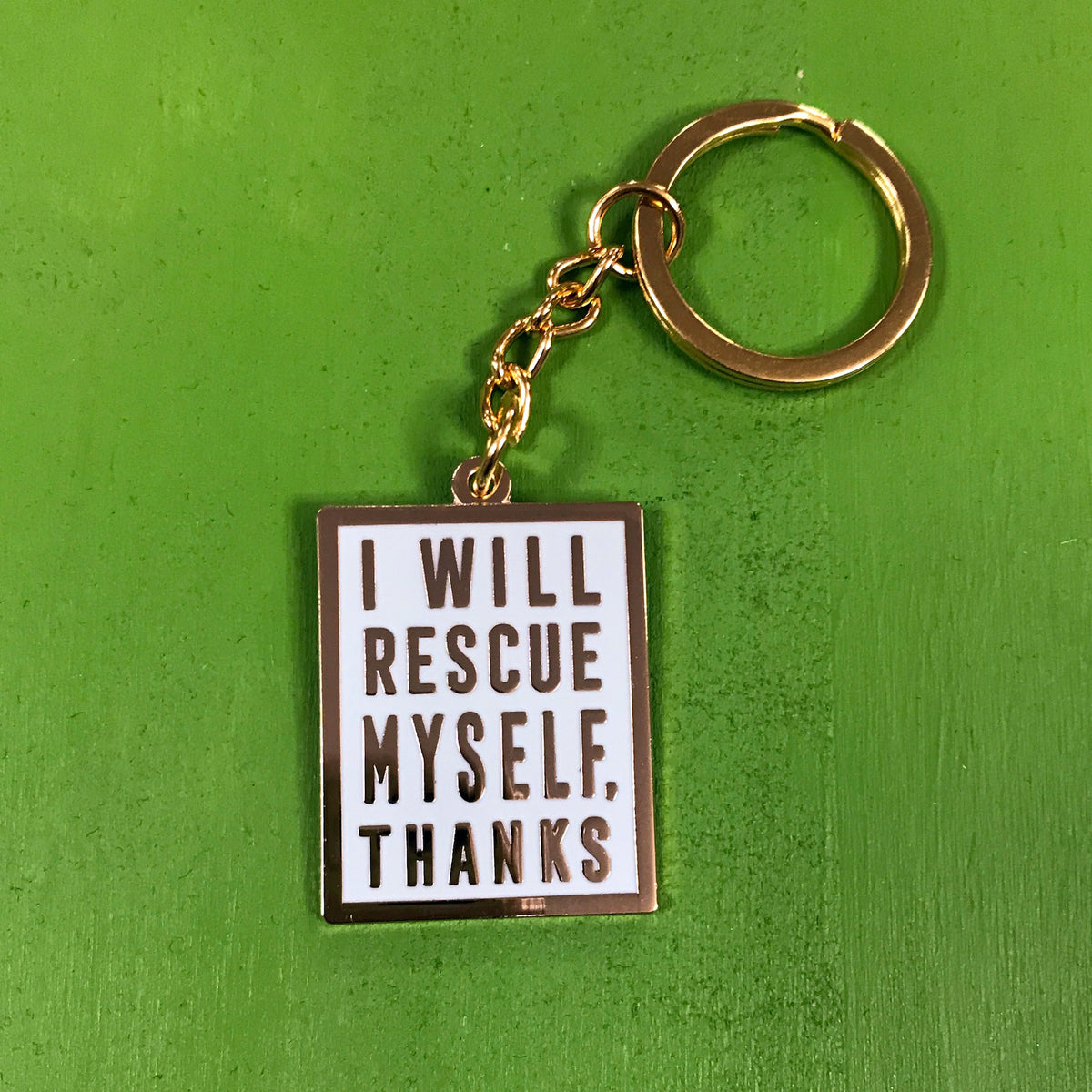 A mint-colored keychain with gold hardware and gold text that says "I will rescue myself, thanks" against a green background