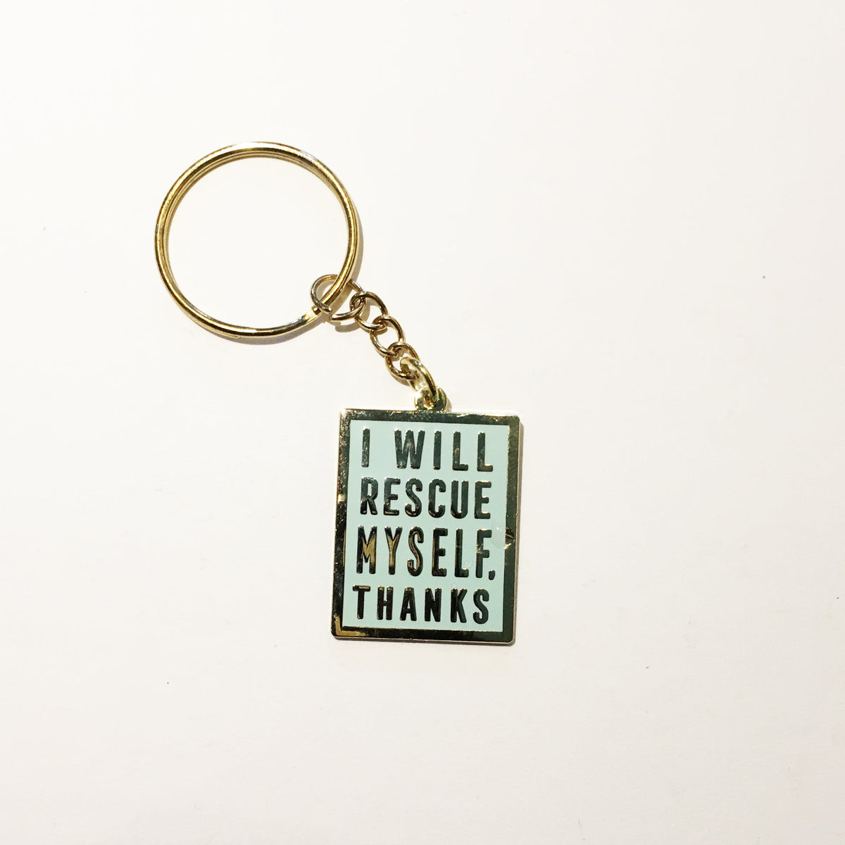 A mint colored keychain with gold hardware, a gold border, and gold text that says "I will rescue myself, thanks" against a white background. 